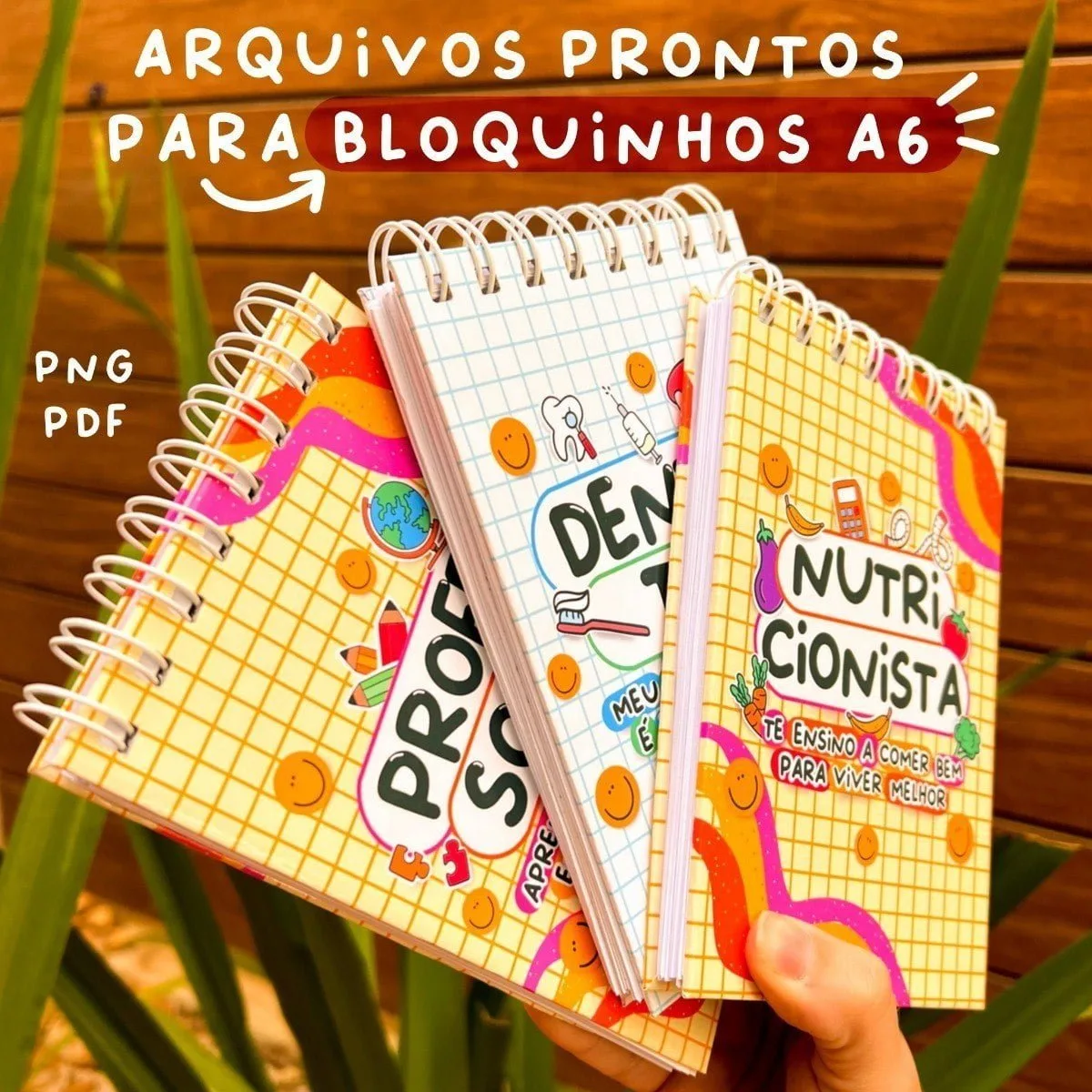 Tres pequenos cadernos espiralados com capas coloridas ilustradas sobre fundo de madeira.