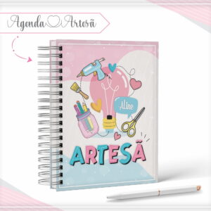 Caderno espiral com capa rosa decorada com desenhos de materiais de artesanato.