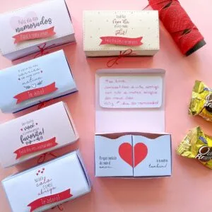 Caixas de presente decoradas com mensagens românticas dispostas sobre uma superfície rosa.