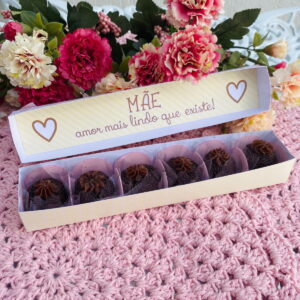 Caixa aberta com brigadeiros decorados sobre uma toalha rosa de crochê com flores.