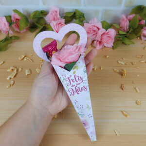 Mão segurando suporte em formato de cone com flor rosa e doce