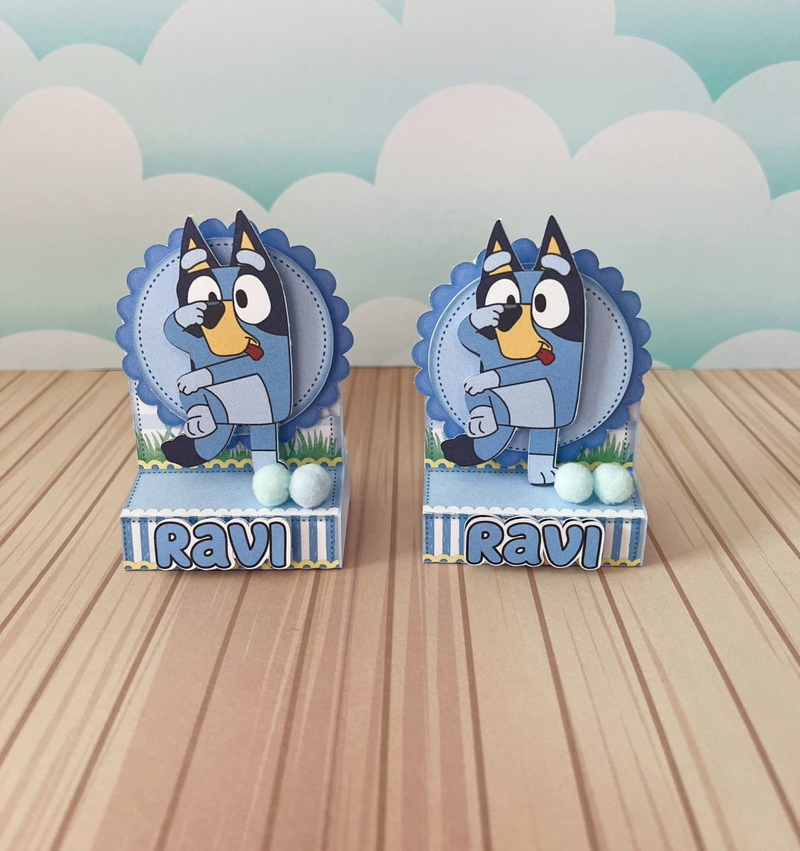 Arquivo de Corte Festa Bluey para Silhouette e Cricut 3 Duas caixinhas personalizadas de papel com tema de cachorro azul sobre mesa listrada.