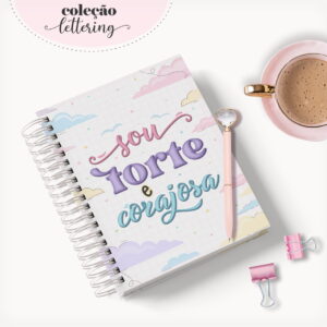 Caderno espiral com capa ilustrada, caneta rosa, xícara de café e clipes em fundo branco