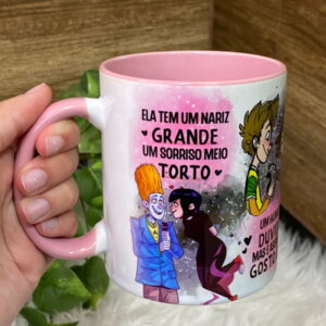 Caneca branca e rosa com arte digital colorida, sendo segurada por uma mão.