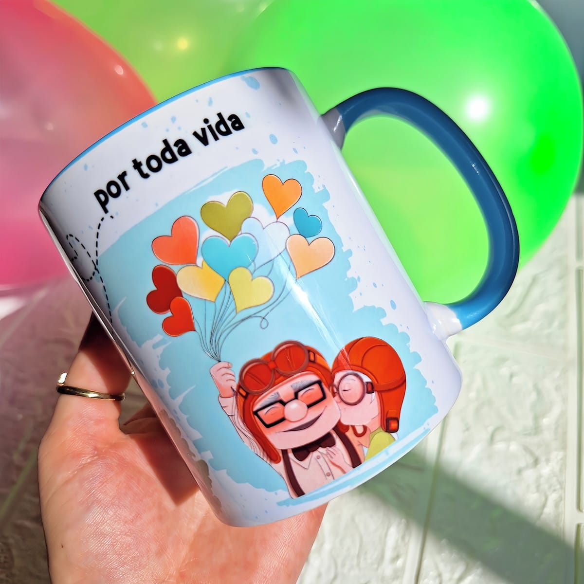 Arte Digital Caneca Up Altas Aventuras PNG do Carl e Ellie 3 Caneca branca com ilustração de casal e balões de coração coloridos em um fundo desfocado.