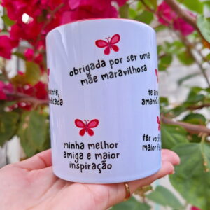 Mão segurando caneca branca estampada com textos e borboletas rosas