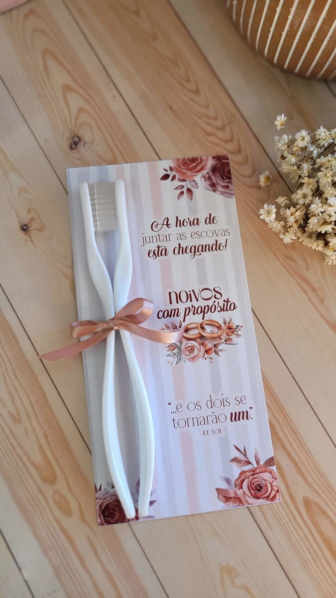 Baixe Kit Digital Dia dos Namorados com Mimos Aquarela 2 Duas escovas de dente brancas unidas por fita rosa sobre um cartão de casamento.
