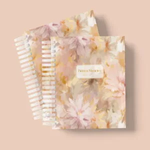 Dois cadernos espiralados com estampa floral em tons pastéis e texto centralizado.