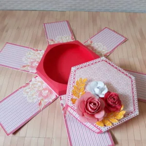 Caixa artesanal vermelha e rosa aberta com abas decoradas com flores.