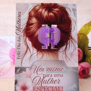 Presilha de cabelo roxa apoiada em cartão com ilustração de mulher.