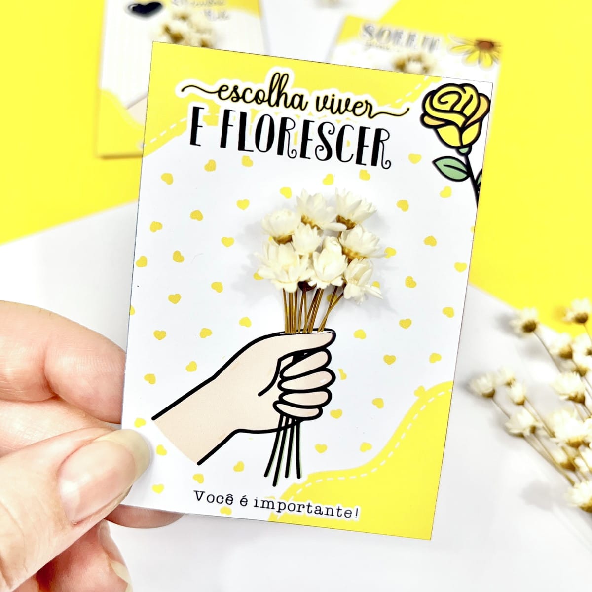 Card Setembro Amarelo PNG e PDF para Imprimir 3 Mão segurando cartão branco com flores secas e mensagem motivacional.
