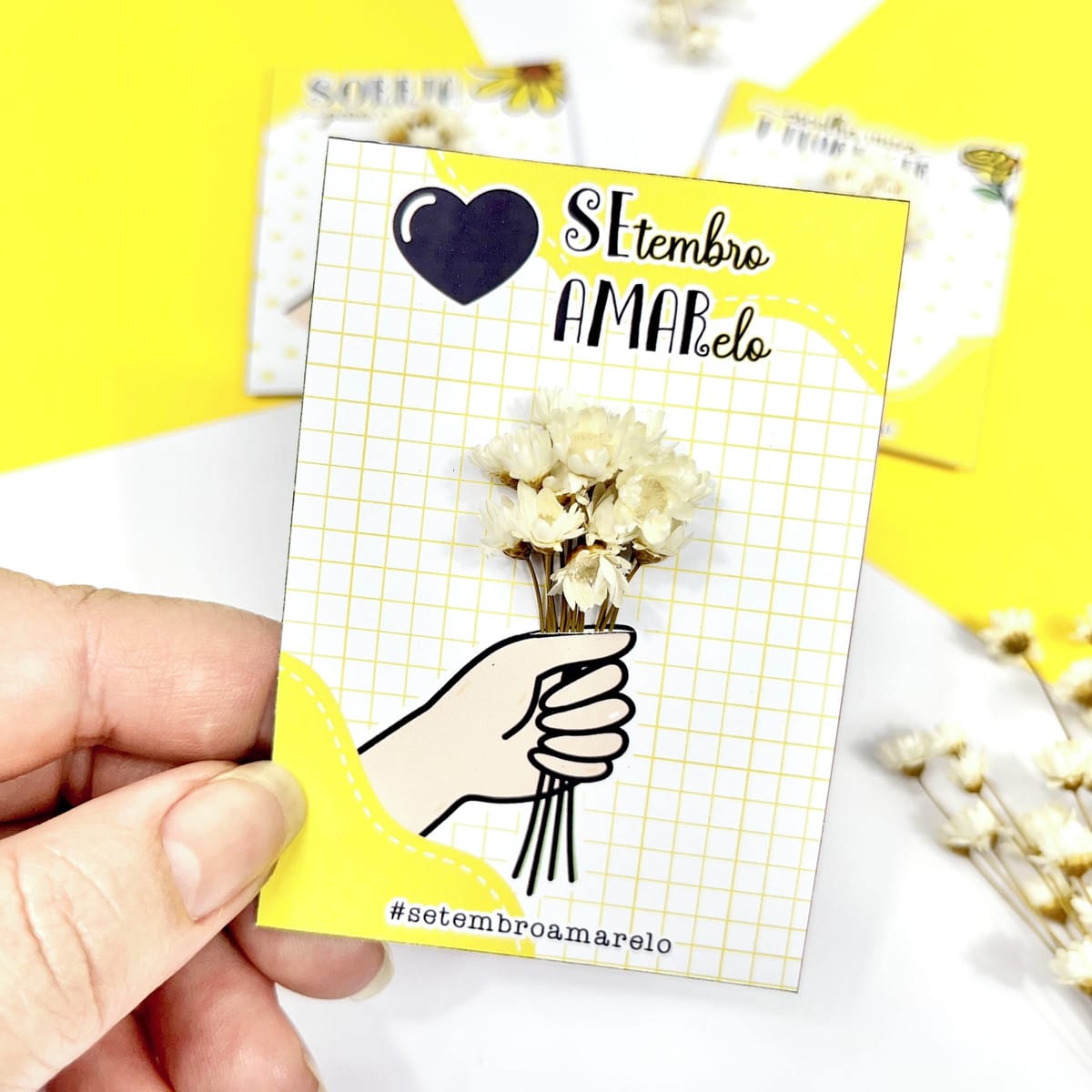 Card Setembro Amarelo PNG e PDF para Imprimir 5 Design de cartão amarelo e branco com ilustração de mão segurando flores.