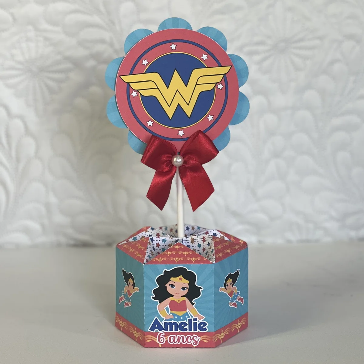 Centro de mesa decorativo com estampa de heroína e um laço vermelho.