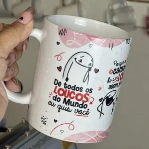 Mão segurando caneca branca estampada com desenho romântico e frase em português.