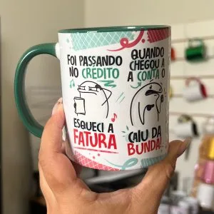 Mão segurando uma caneca branca estampada com desenhos e textos divertidos.