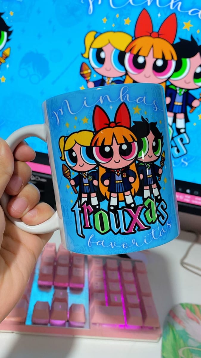 Estampa Meninas Super Poderosas Bruxinhas para Caneca PNG 3 Mão segura caneca azul claro com personagens de desenho animado e texto colorido.