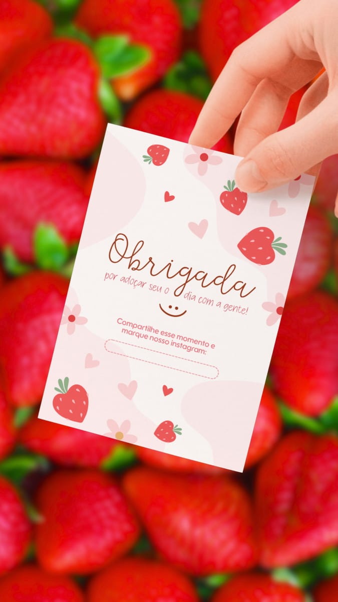 Kit Adesivos e Tags Morango Amor para Embalagem no Canva 5 Mão segurando cartão decorado com tema de morangos e fundo de morangos reais.