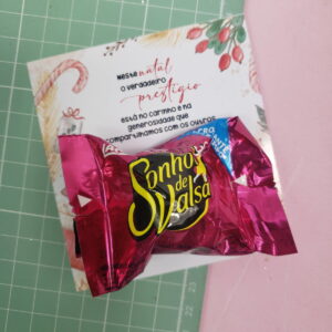 Dois bombons embalados em papel rosa escuro sobre um cartão comemorativo decorado.