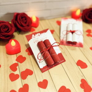 Dois pergaminhos vermelhos em cartão, corações, rosas e velas decoram celebração romântica.