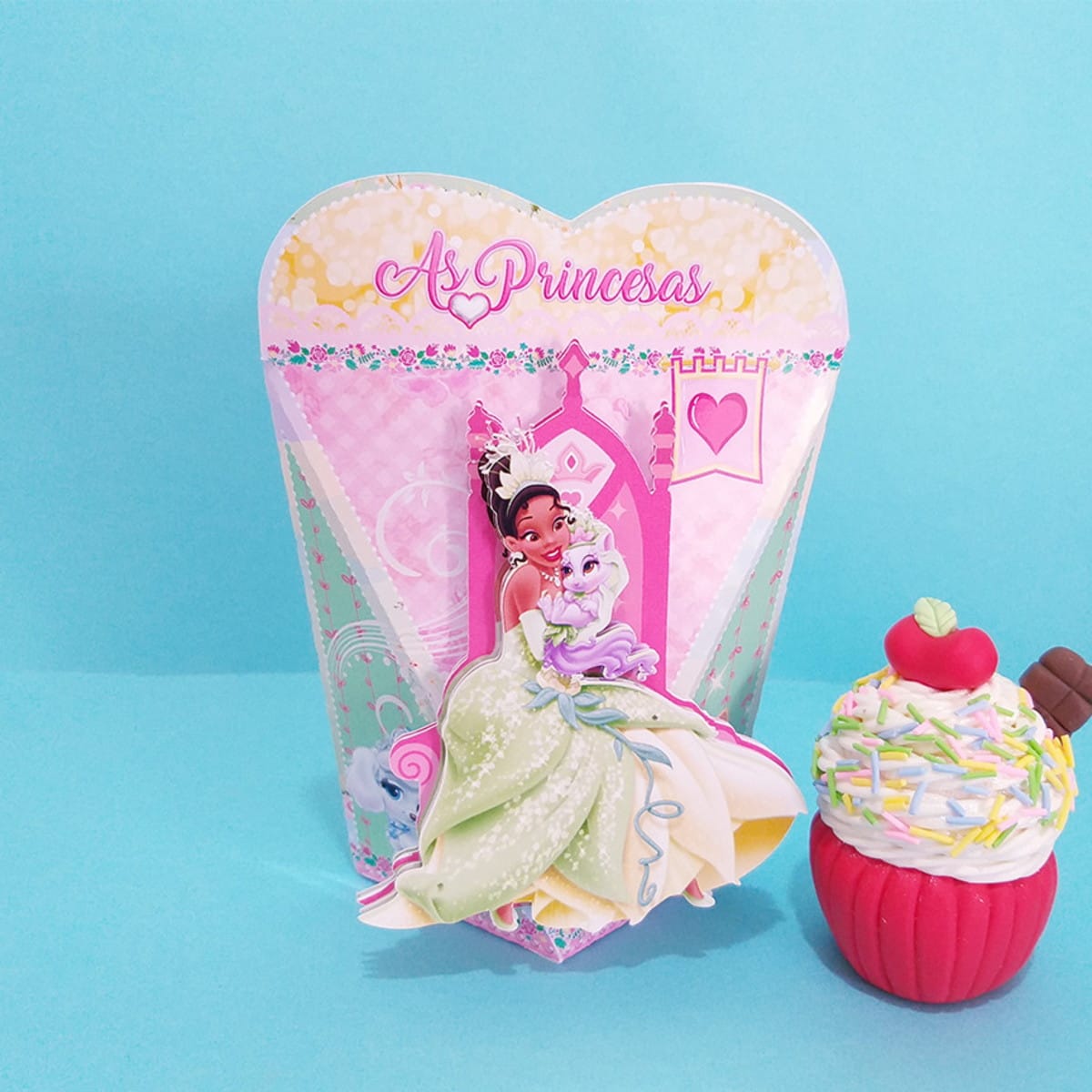 Kit digital festa Princesas Disney com moldes de corte 2 Caixa decorativa com ilustração de princesa e gato, ao lado de um cupcake decorativo.