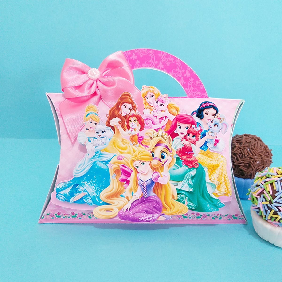 Kit digital festa Princesas Disney com moldes de corte 4 Caixa de presente rosa com arte de princesas e animais, laço de fita, em fundo azul.