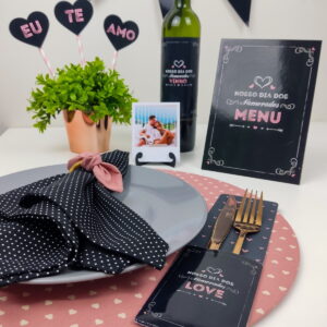 Mesa posta decorada com temática romântica contendo prato, talheres, bebida e placas decorativas.