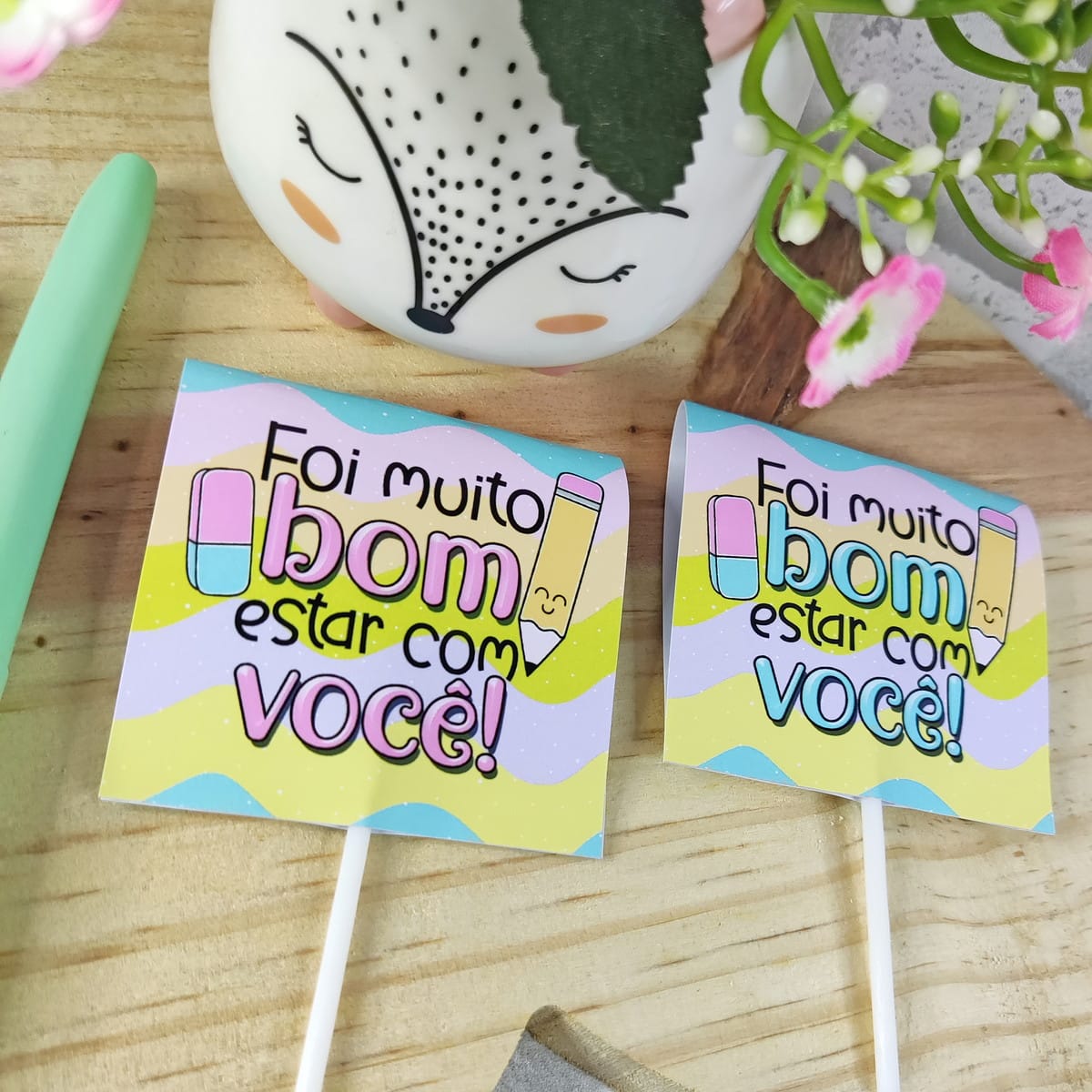 Kit digital mimos formatura escolar com arquivos PNG 4 Dois toppers de papel coloridos com frase escrita em fundo decorado sobre madeira.
