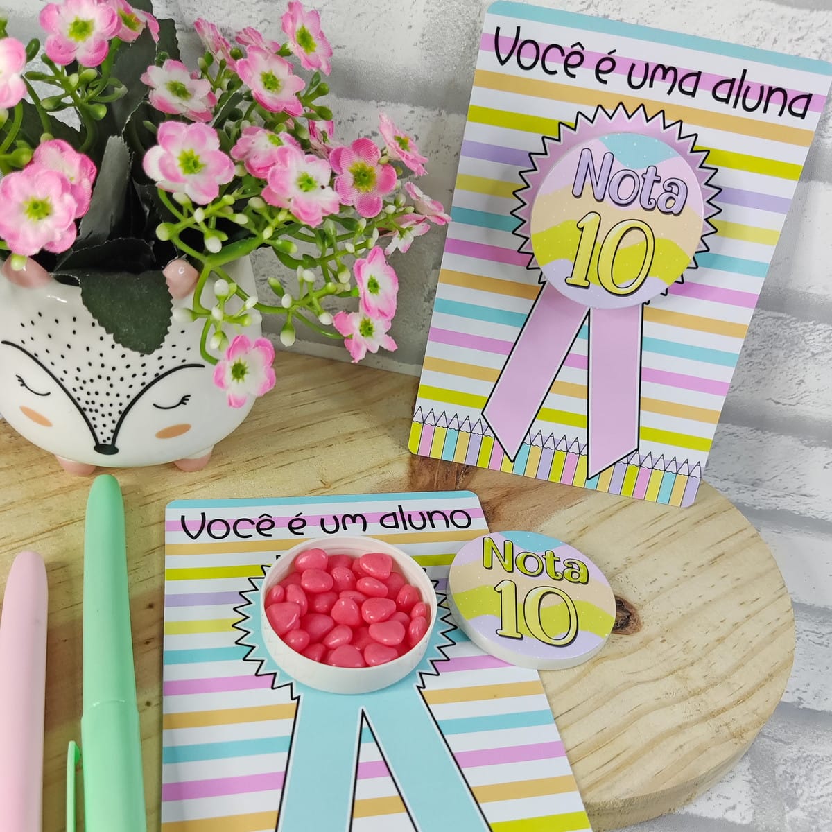 Kit digital mimos formatura escolar com arquivos PNG 1 Cartões coloridos com doces, canetas e vasinho de flores sobre superfície de madeira.