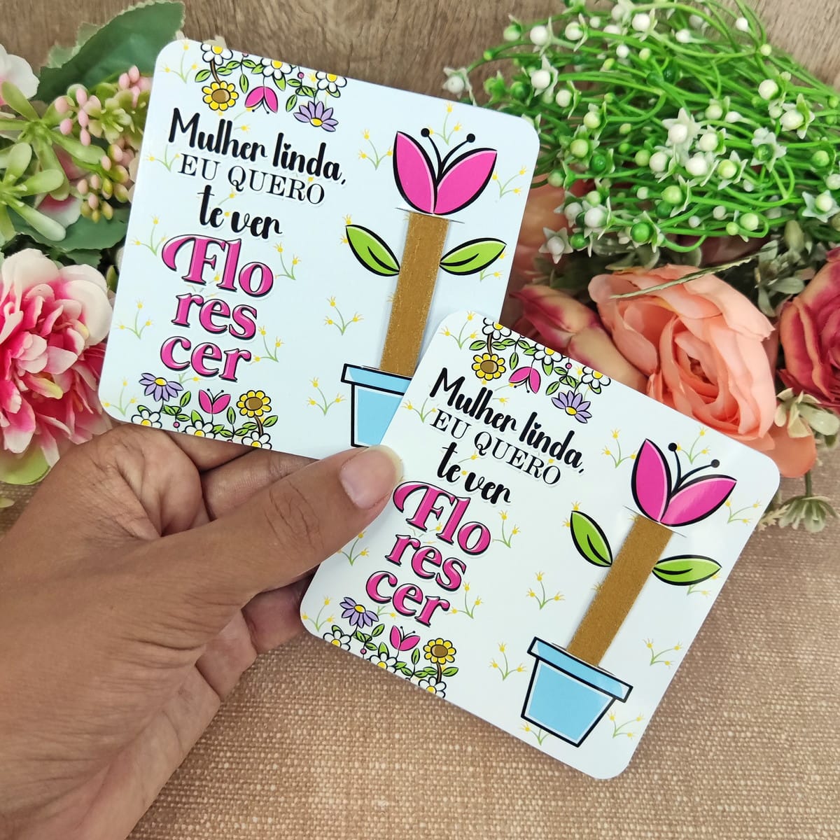 Kit Digital Dia da Mulher para montar mimos e lembrancinhas 3 Duas tags brancas com ilustração floral e frase motivacional, seguradas por uma mão.
