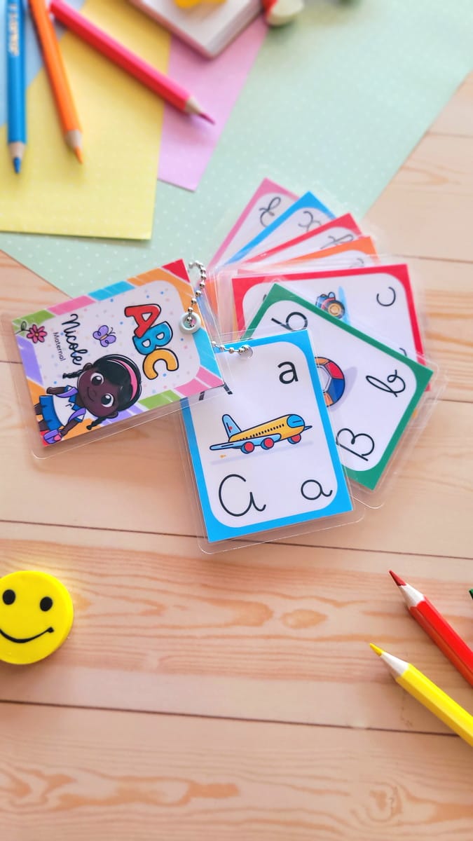 Kit Digital Volta às Aulas com 200 Ilustrações Escolares 2 Cartões educacionais com letras e ilustrações coloridas sobre uma mesa de madeira clara.
