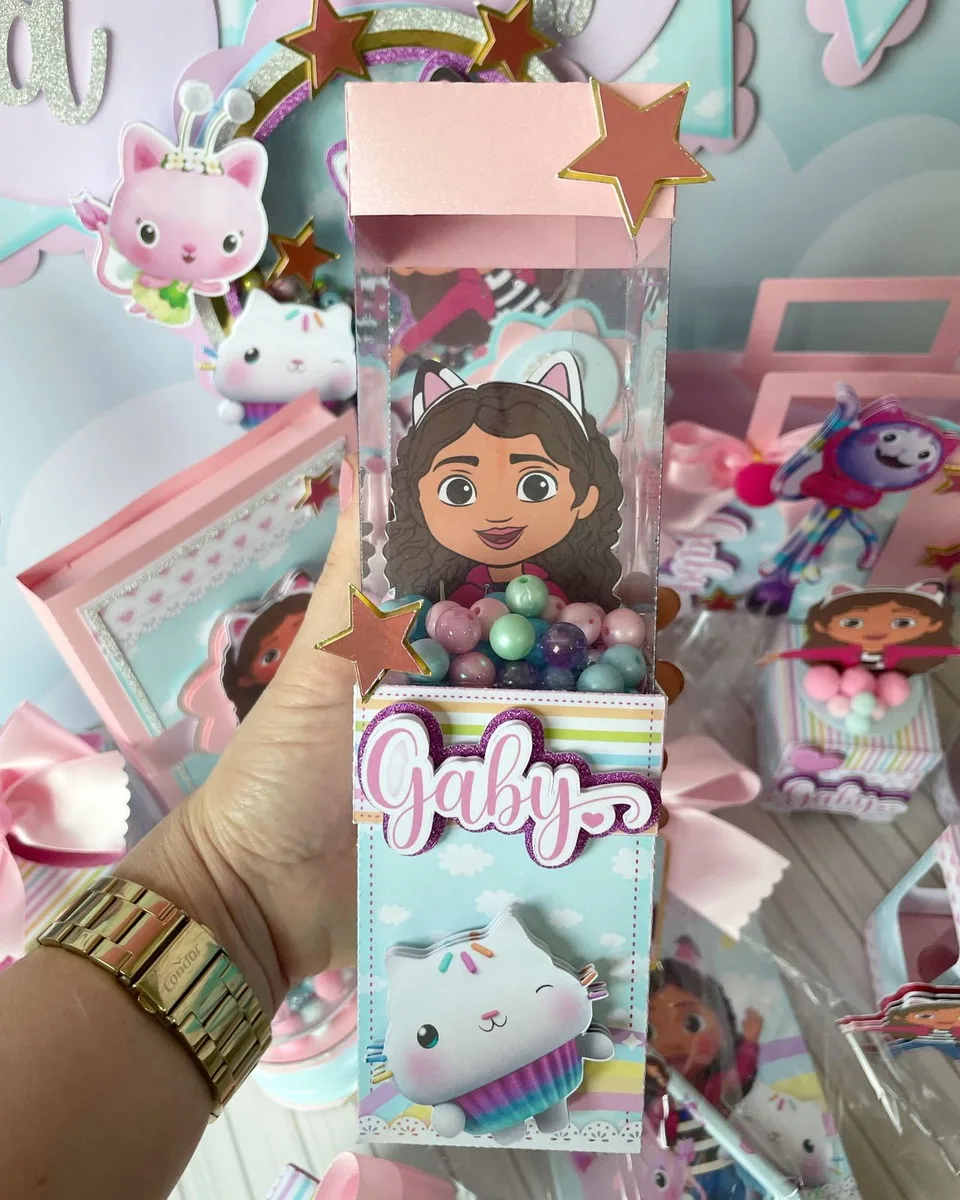 Mão segurando caixa de lembrancinha personalizada com personagem e miçangas coloridas