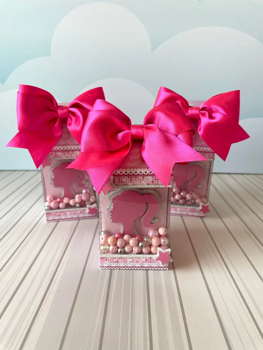 Kit Festa Barbie Luxo - Arquivo Digital 4 Três caixas decorativas rosa contendo pérolas e laços grandes no topo sobre mesa listrada.