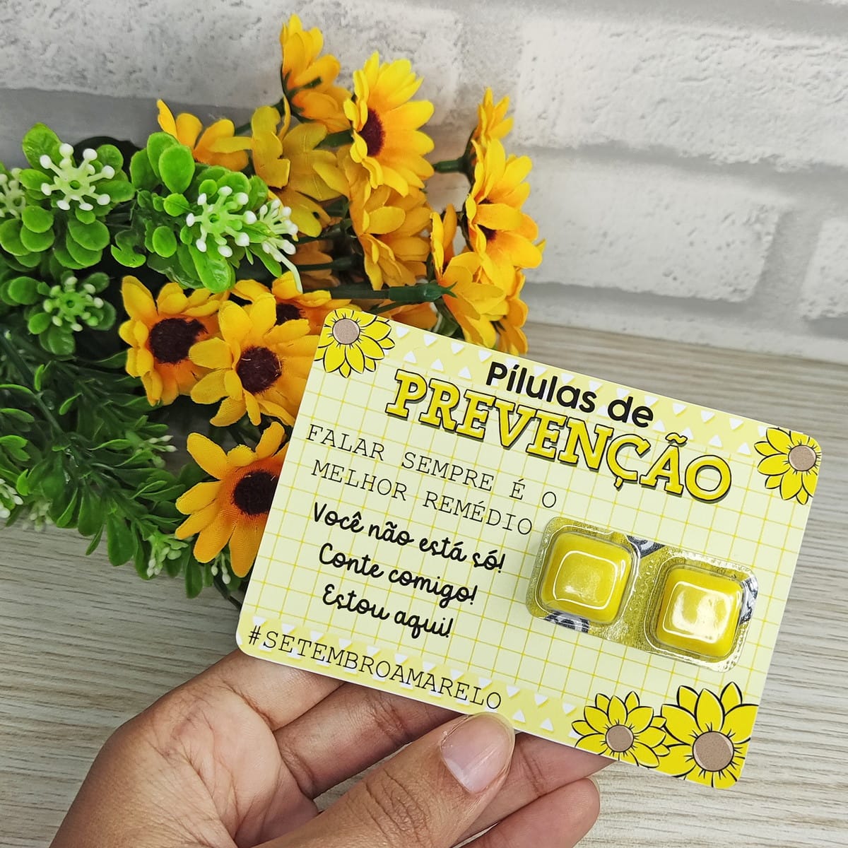 Kit Setembro Amarelo Digital pronto para Imprimir 4 Mão segurando cartão amarelo com "Pílulas de Prevenção" e girassóis.