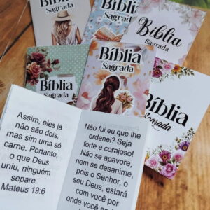 Várias capas de livros chamados Bíblia Sagrada com ilustrações florais sobre uma mesa de madeira.