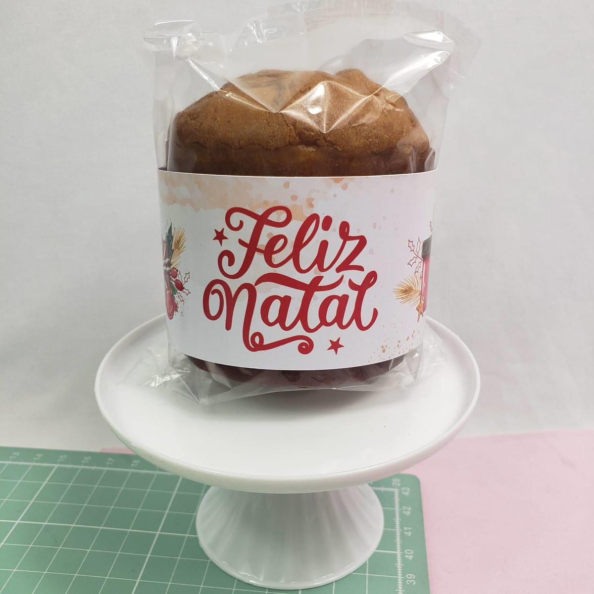 Lembrancinhas de Natal para Clientes prontas para Imprimir 3 Panetone embalado com rótulo personalizado de Feliz Natal sobre suporte branco.