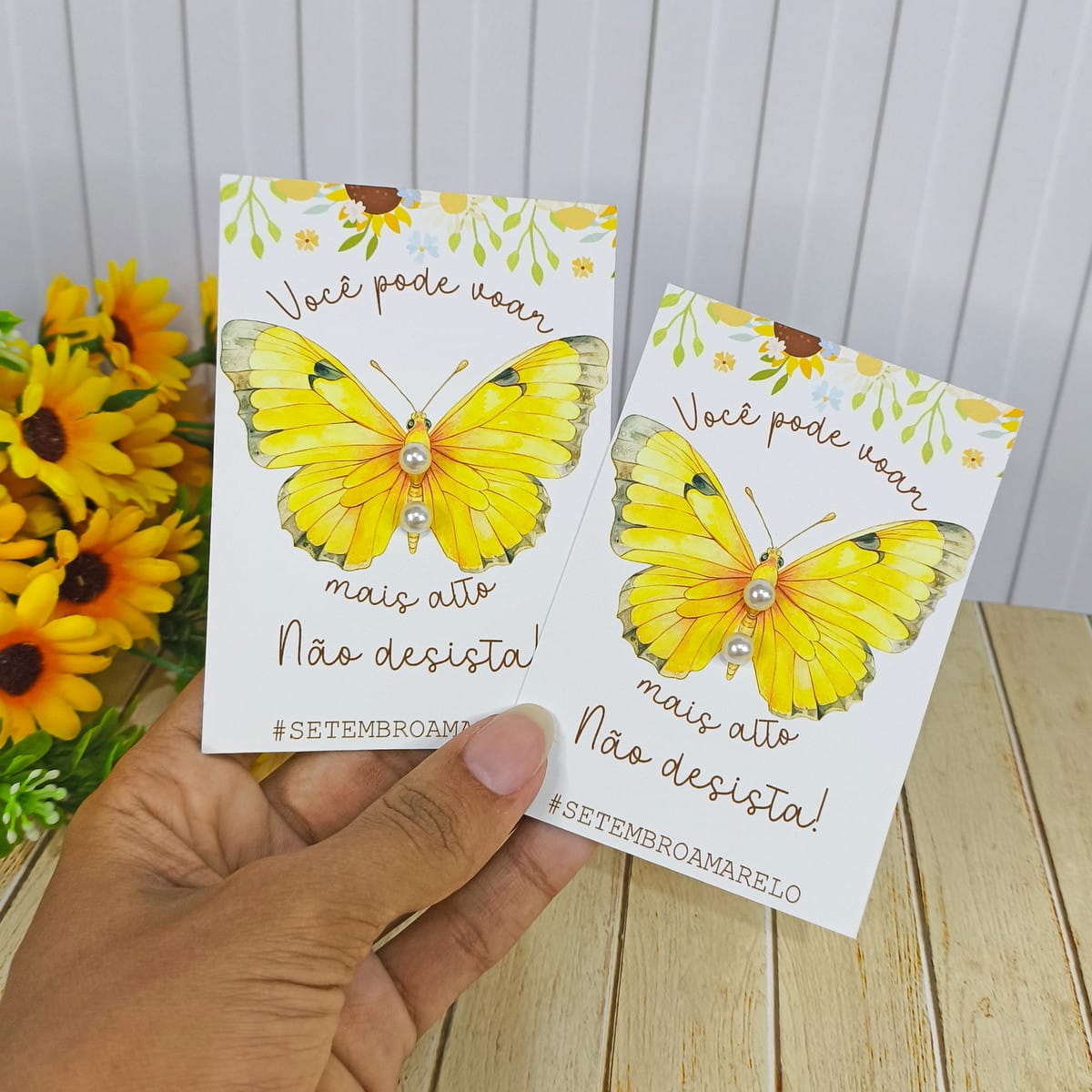 Kit Digital Setembro Amarelo Lembrancinhas em PNG 2 Mão segura dois cartões brancos com borboleta amarela e pérolas decorativas.