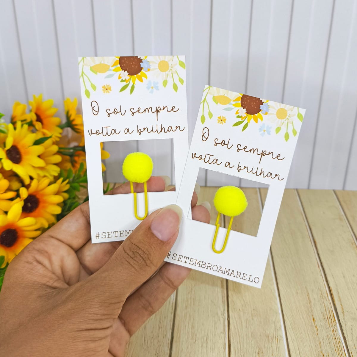 Kit Digital Setembro Amarelo Lembrancinhas em PNG 3 Mão segurando dois cartões com frase "O sol sempre volta a brilhar" e clipes amarelos.