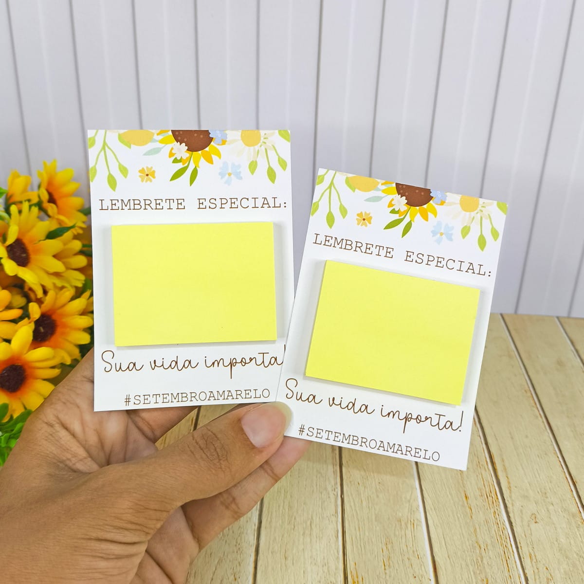 Kit Digital Setembro Amarelo Lembrancinhas em PNG 4 Duas mãos segurando cartões com lembretes amarelos e girassóis visíveis.