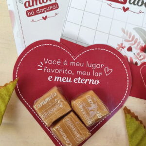 Cartão vermelho em formato de coração com doces de caramelo e mensagens românticas.