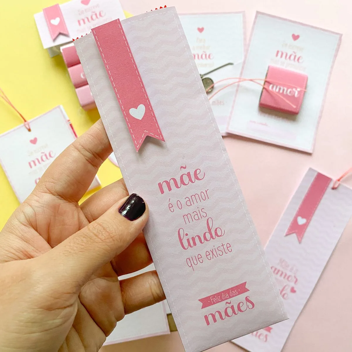 Mão segurando marcador de página rosa decorado com texto temático e corações