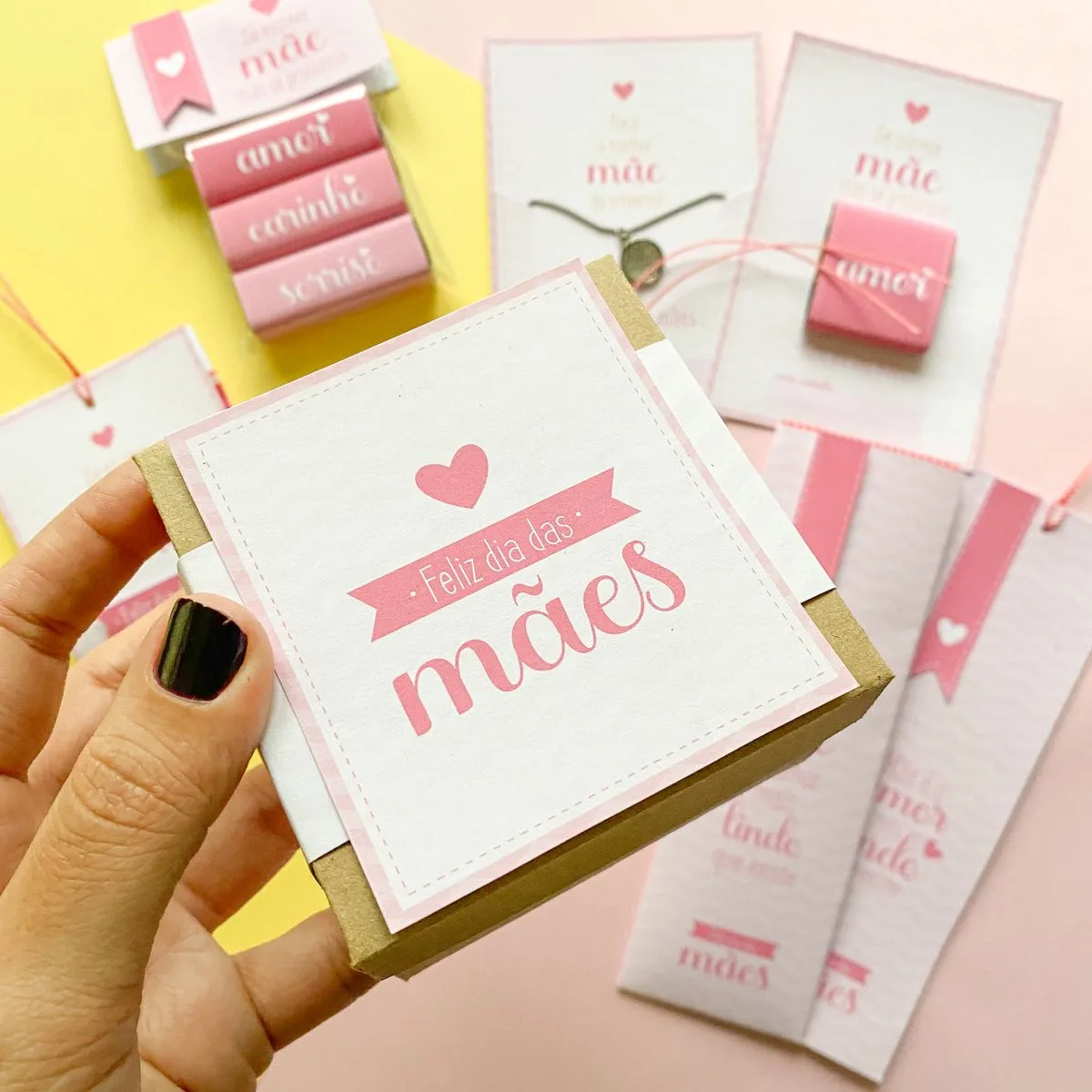 Mão segurando pequena caixa marrom com arte rosa em relevo e doces.