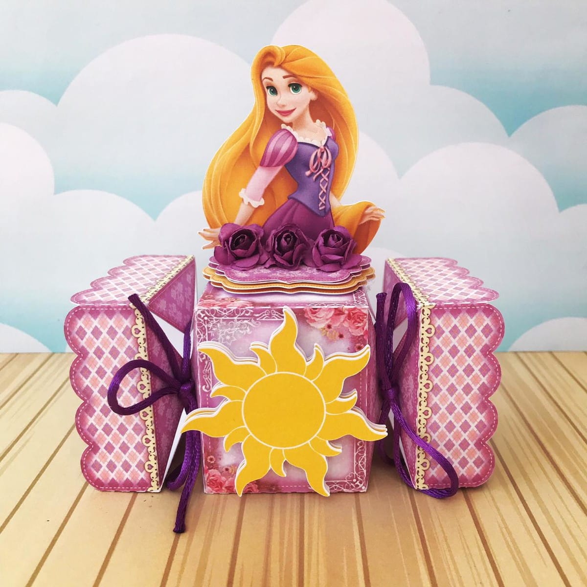 Kit Digital Festa Rapunzel com Caixas Sacolas e Convites 2 Personagem feminina de desenho animado com cabelo loiro em cima de caixas decoradas.