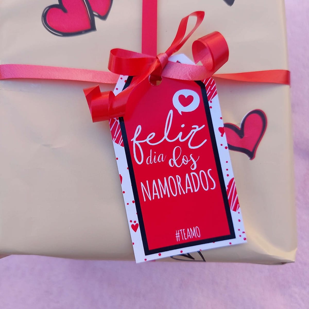 Tag Dia dos Namorados em PDF para Imprimir 1 Um presente embrulhado com papel dourado, laço vermelho e tag "Feliz Dia dos Namorados".